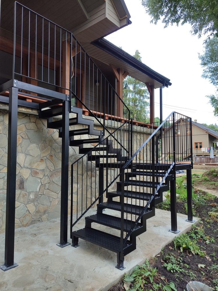 Escalier extérieur métallique noir avec garde-corps barreaux sur mur en pierre