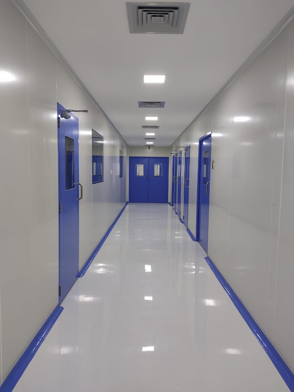Sol époxy blanc immaculé dans couloir de salle blanche avec portes bleues
